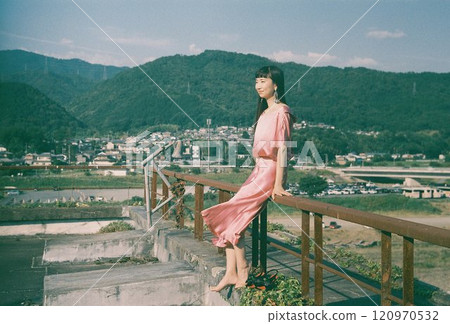 Barefoot woman in pink dress poses with a view on an abandoned rooftop 120970532