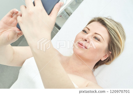 Caucasian mature woman relaxing and taking selfie in spa setting with smartphone Caucasian mature woman relaxing and taking selfie in spa setting with smartphone 120970701