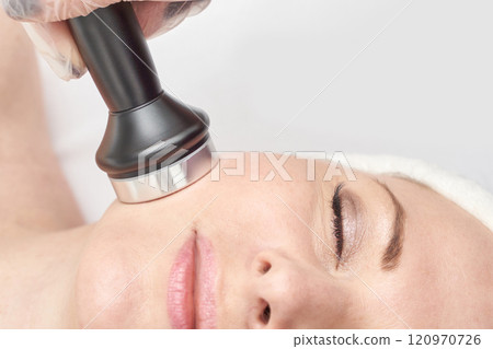 Caucasian female undergoing facial treatment with beauty device for skin 120970726