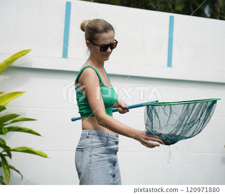A young woman clean leaves out of a pool A young woman clean leaves out of a pool 120971880
