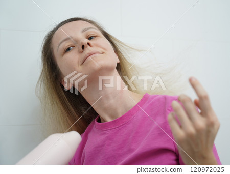 A woman is expertly styling her hair using a blow dryer and brush while in the bathroom A woman is expertly styling her hair using a blow dryer and brush while in the bathroom 120972025