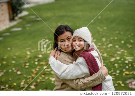 Young granddaughter with gradmother hugging, standing in garden. Young granddaughter with gradmother hugging, standing in garden. 120972031