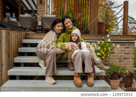 Mature daughter, grandmother and granddaugter sitting on wooden stairs, hugging. Mother's day and multigenerational family concept. Mature daughter, grandmother and granddaugter sitting on wooden stairs, hugging. Mother's day and multigenerational family concept. 120972032