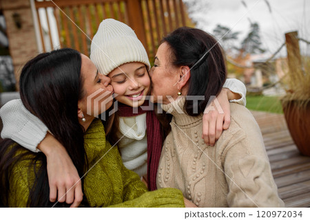 Mature daughter, grandmother and granddaugter sitting on wooden patio, hugging. Mother's day and multigenerational family concept. 120972034