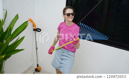A woman raking the lawn at the backyard of her house A woman raking the lawn at the backyard of her house 120972053