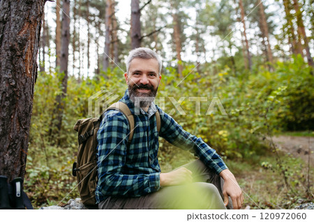 Handsome man sitting on rock in the middle of nature, enjoying peaceful atmosphere of the forest, forestbathing. 120972060