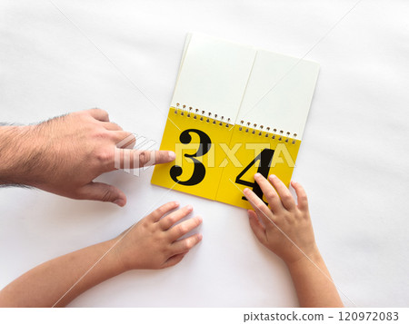 Parent and child learning numbers together with a yellow flip book 120972083