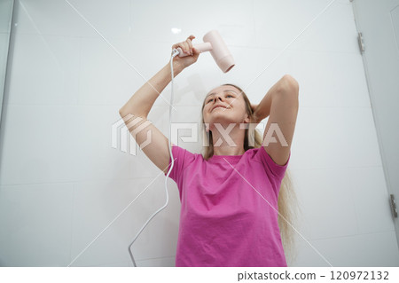 A woman is expertly styling her hair using a blow dryer and brush while in the bathroom 120972132
