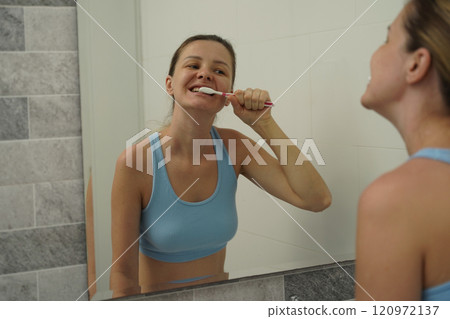 Young woman in a modern bathroom washing her face and brushing her teeth Young woman in a modern bathroom washing her face and brushing her teeth 120972137