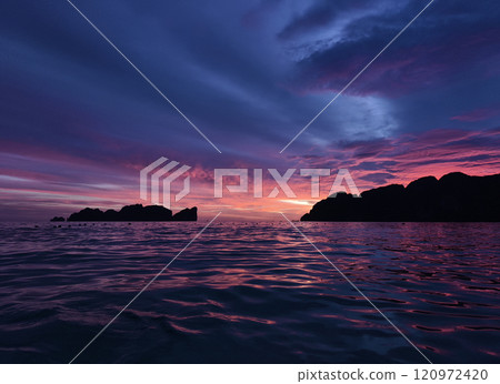 A stunning sunset is casting vibrant hues of color over a tranquil ocean 120972420