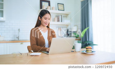 Beautiful young Asian woman working with laptop computer in home kitchen. Work at home 120972450