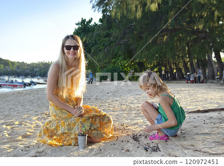 A mother and her daughter as they collect shells together A mother and her daughter as they collect shells together 120972451