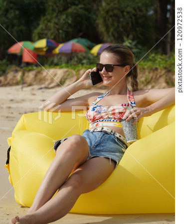 A young woman on the beach lounging on a yellow bean bag  120972538