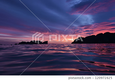 A stunning sunset is casting vibrant hues of color over a tranquil ocean 120972825