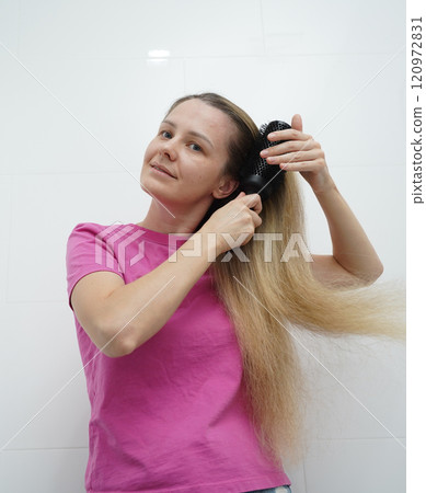 A woman is expertly styling her hair using a blow dryer and brush while in the bathroom 120972831