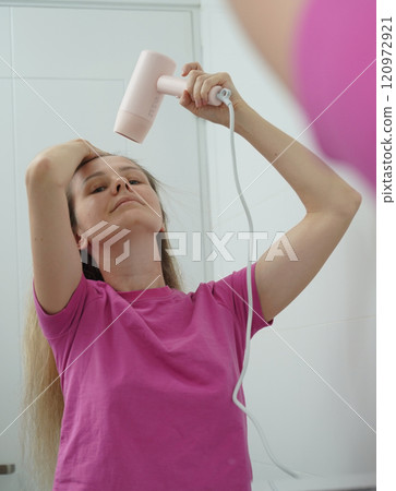 A woman is expertly styling her hair using a blow dryer and brush while in the bathroom 120972921