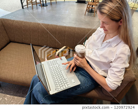 A young woman enjoys coffee while working on her laptop  120972924
