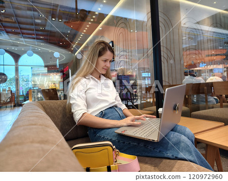 A young woman enjoys coffee while working on her laptop  120972960