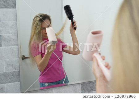 A woman is expertly styling her hair using a blow dryer and brush while in the bathroom A woman is expertly styling her hair using a blow dryer and brush while in the bathroom 120972966