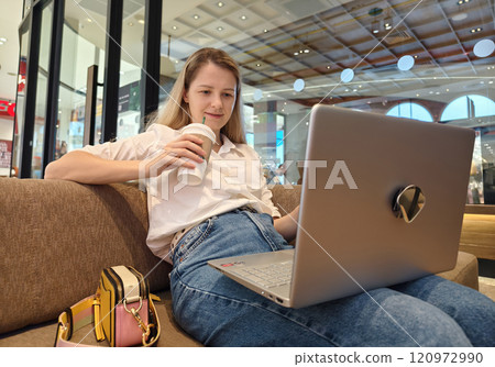 A young woman enjoys coffee while working on her laptop A young woman enjoys coffee while working on her laptop 120972990