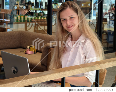 A young woman enjoys coffee while working on her laptop  120972993