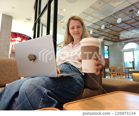 A young woman enjoys coffee while working on her laptop A young woman enjoys coffee while working on her laptop 120973134