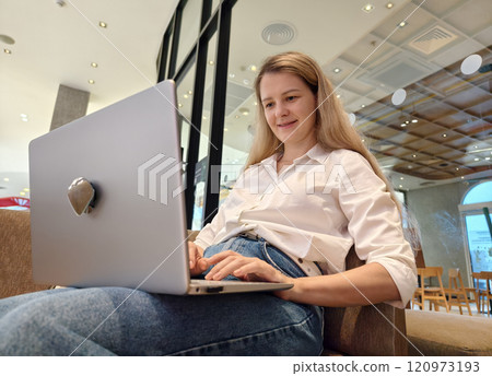 A young woman enjoys coffee while working on her laptop  120973193
