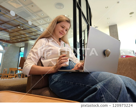 A young woman enjoys coffee while working on her laptop A young woman enjoys coffee while working on her laptop 120973224