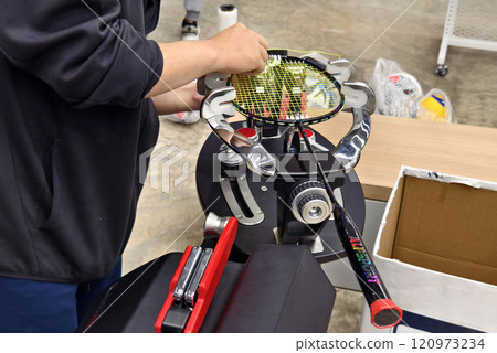 Strings a badminton racket on a racket stringing machine. Strings a badminton racket on a racket stringing machine. 120973234