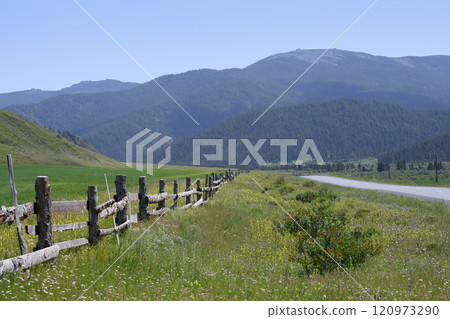 An old wooden fence in a meadow at the foot of the mountains in the Altai Mountains in summer 120973290