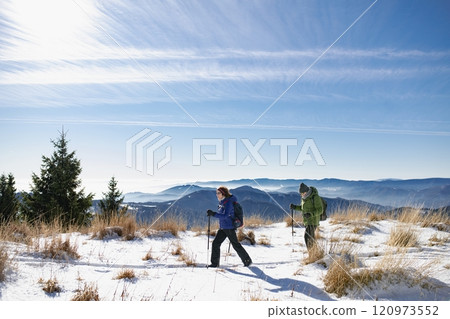 Active seniors walking through snowy winter nature. Romantic winter hike for an elderly couple in snowy mountains. Active seniors walking through snowy winter nature. Romantic winter hike for an elderly couple in snowy mountains. 120973552