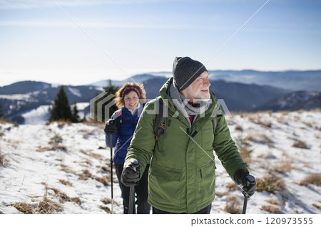 Winter hike for an elderly man and his wife in snowy mountains. Active seniors enjoying nature. 120973555