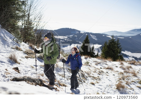Active seniors walking through snowy winter nature. Romantic winter hike for an elderly couple in snowy mountains. 120973560