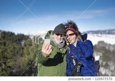 Active seniors resting during hike in winter nature, taking selfie. Romantic winter hike for an elderly couple in snowy mountains. 120973570