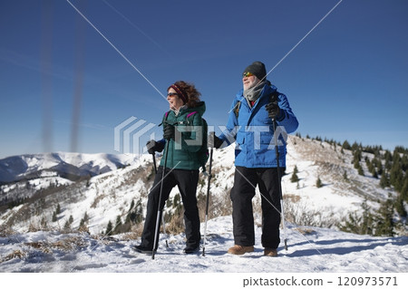 Active seniors walking through snowy winter nature. Romantic winter hike for an elderly couple in snowy mountains. Active seniors walking through snowy winter nature. Romantic winter hike for an elderly couple in snowy mountains. 120973571