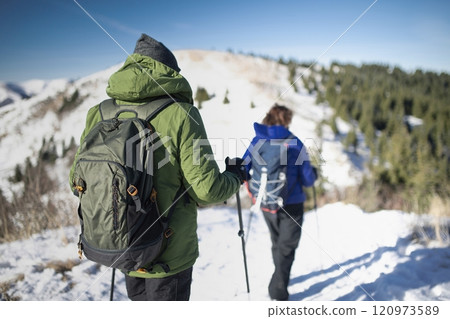 Rear view of active seniors walking through a winter nature. Romantic winter hike for an elderly couple in snowy mountains. 120973589