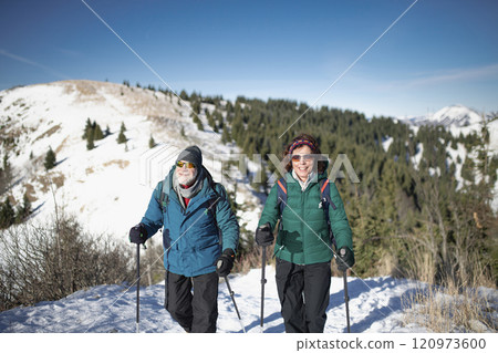 Active seniors walking through snowy winter nature. Romantic winter hike for an elderly couple in snowy mountains. Active seniors walking through snowy winter nature. Romantic winter hike for an elderly couple in snowy mountains. 120973600