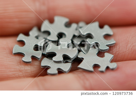 Close-up of a Hand Holding a Collection of Silver Jigsaw Puzzle Pieces, Symbolizing Problem Solving and Cognitive Challenges in Life and Games 120973736