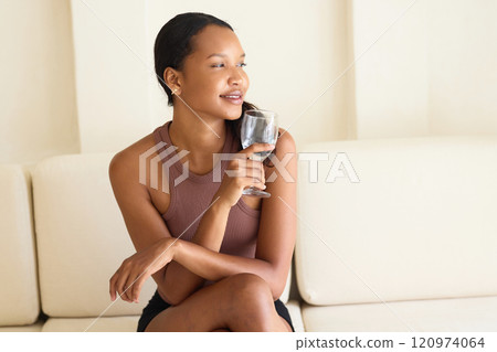 Relaxed Woman Enjoying a Glass of Water on Comfortable Sofa at Home 120974064