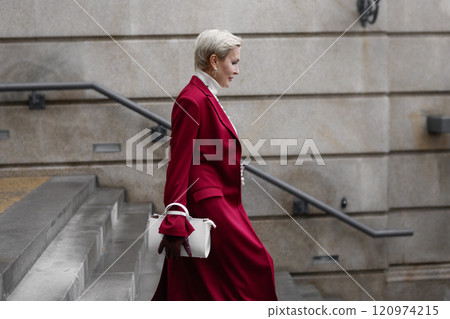 Stylish Woman with Short Haircut in Burgundy Coat Walks City Street, Wearing Fashionable clothing White Turtleneck Sweater, White Bag. Confident and Chic Mature Fashion Model Stylish Woman with Short Haircut in Burgundy Coat Walks City Street, Wearing Fashionable clothing White Turtleneck Sweater, White Bag. Confident and Chic Mature Fashion Model 120974215