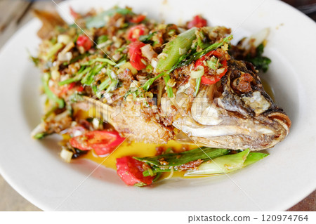 Deep fried sea bass topped with fresh bird eye chilli and vegetable ingredient on white dish 120974764