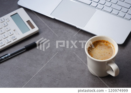 Image of a man working at his desk with a calculator and laptop while drinking freshly brewed coffee (cafe latte) 120974999