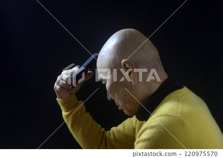 The troubled face of an old man with a shaved head holding a smartphone The troubled face of an old man with a shaved head holding a smartphone 120975570