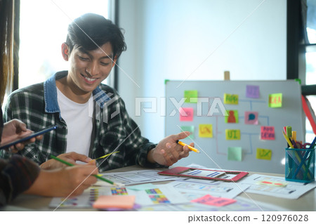 Cheerful young man collaborating with his team on app design and UI UX development in the office 120976028
