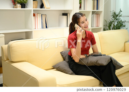 Young woman in a red shirt having pleasant phone conversation on sofa at home Young woman in a red shirt having pleasant phone conversation on sofa at home 120976029