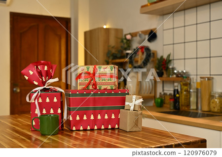 Beautiful Christmas gifts and green coffee mug on wooden kitchen counter with warm light 120976079