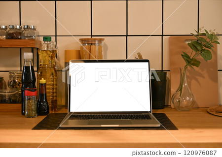 Laptop with blank screen on kitchen countertop surrounded by cooking essentials and decorative plant Laptop with blank screen on kitchen countertop surrounded by cooking essentials and decorative plant 120976087