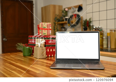 Laptop with blank screen on wooden kitchen table in front of Christmas presents 120976094