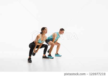 Athletic young man and woman with fit bodies training, doing exercises with kettlebell, showing strength and endurance against white studio background Athletic young man and woman with fit bodies training, doing exercises with kettlebell, showing strength and endurance against white studio background 120977219