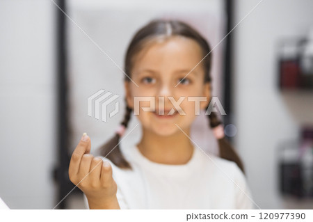 Portrait of young Caucasian girl showing freshly fallen baby tooth while looking into mirror in bathroom, expressing pride and excitement. Portrait of young Caucasian girl showing freshly fallen baby tooth while looking into mirror in bathroom, expressing pride and excitement. 120977390